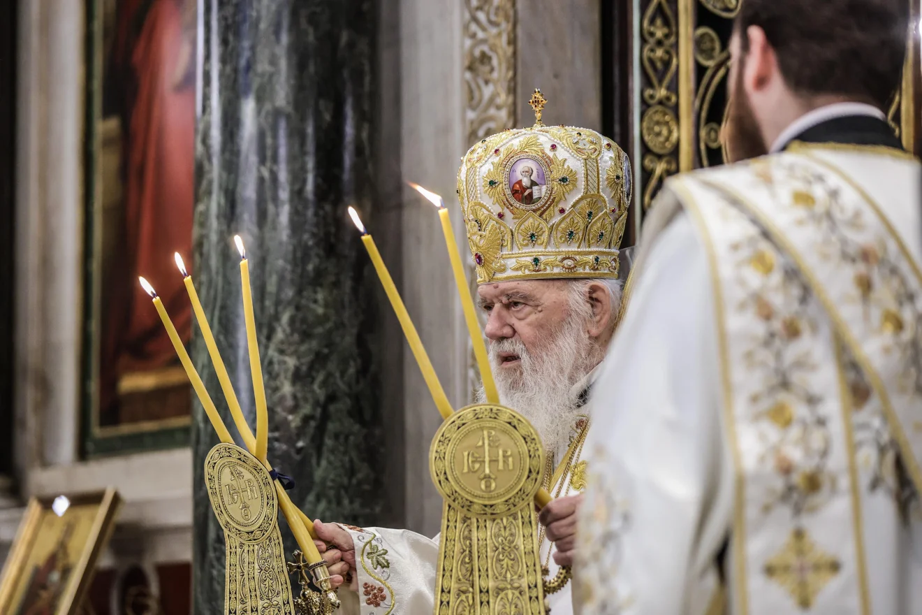 Ο Αρχιεπίσκοπος Ιερώνυμος τελεί θεία λειτουργία, φορώντας επίσημα άμφια και μιλώντας μπροστά στα μικρόφωνα. Η εικόνα αποτυπώνει κατανυκτική στιγμή μέσα στον ναό, με αναμμένες λαμπάδες στο προσκήνιο. Πηγή: INTIME