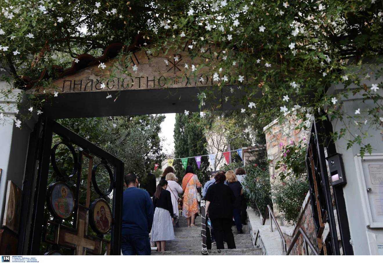 Πιστοί ανεβαίνουν τα σκαλιά προς εκκλησία, περνώντας κάτω από ανθισμένη είσοδο με εικόνες και πυκνή βλάστηση. Πηγή: ΙΝΤΙΜΕ