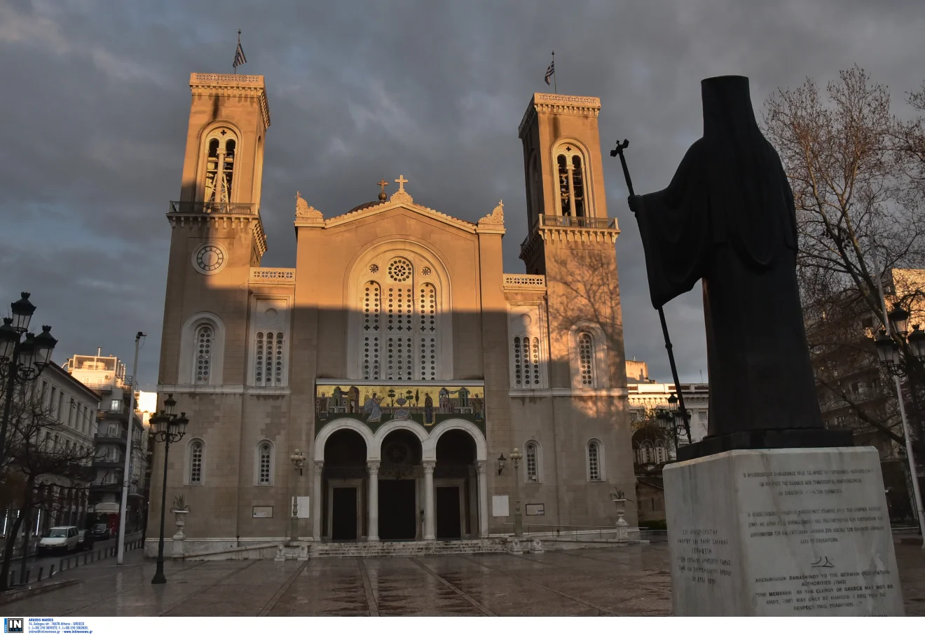 Ο Μητροπολιτικός Ναός Αθηνών φωτισμένος από το φως του ήλιου, με το άγαλμα του Αρχιεπισκόπου Δαμασκηνού σε πρώτο πλάνο και συννεφιασμένο ουρανό. Πηγή: ΙΝΤΙΜΕ