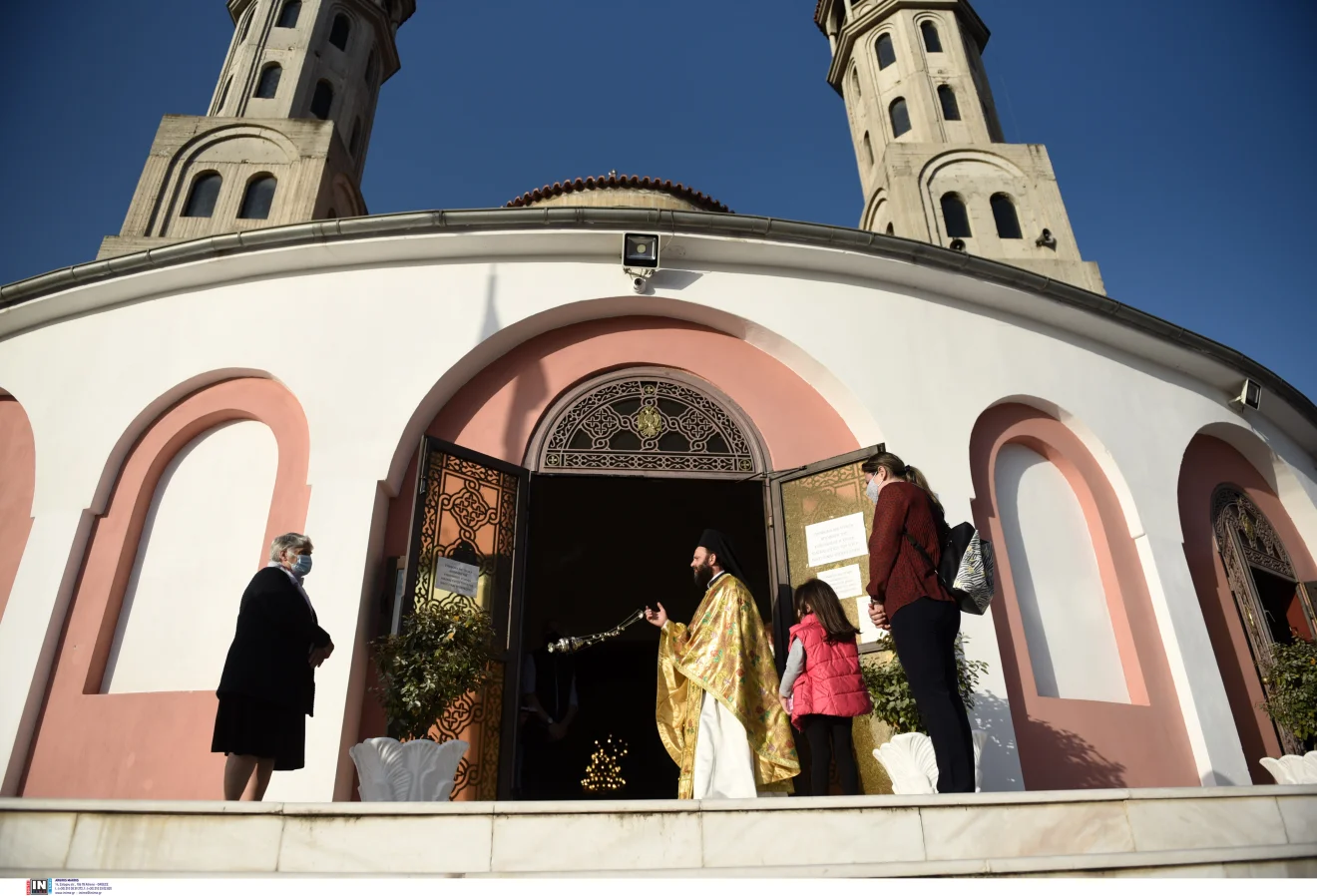 Περιγραφή εικόνας: Ιερέας στην είσοδο ορθόδοξου ναού υποδέχεται πιστούς, με το εορτολόγιο και τις θρησκευτικές ημέρες να βρίσκονται στο επίκεντρο. Πηγή: ΙΝΤΙΜΕ